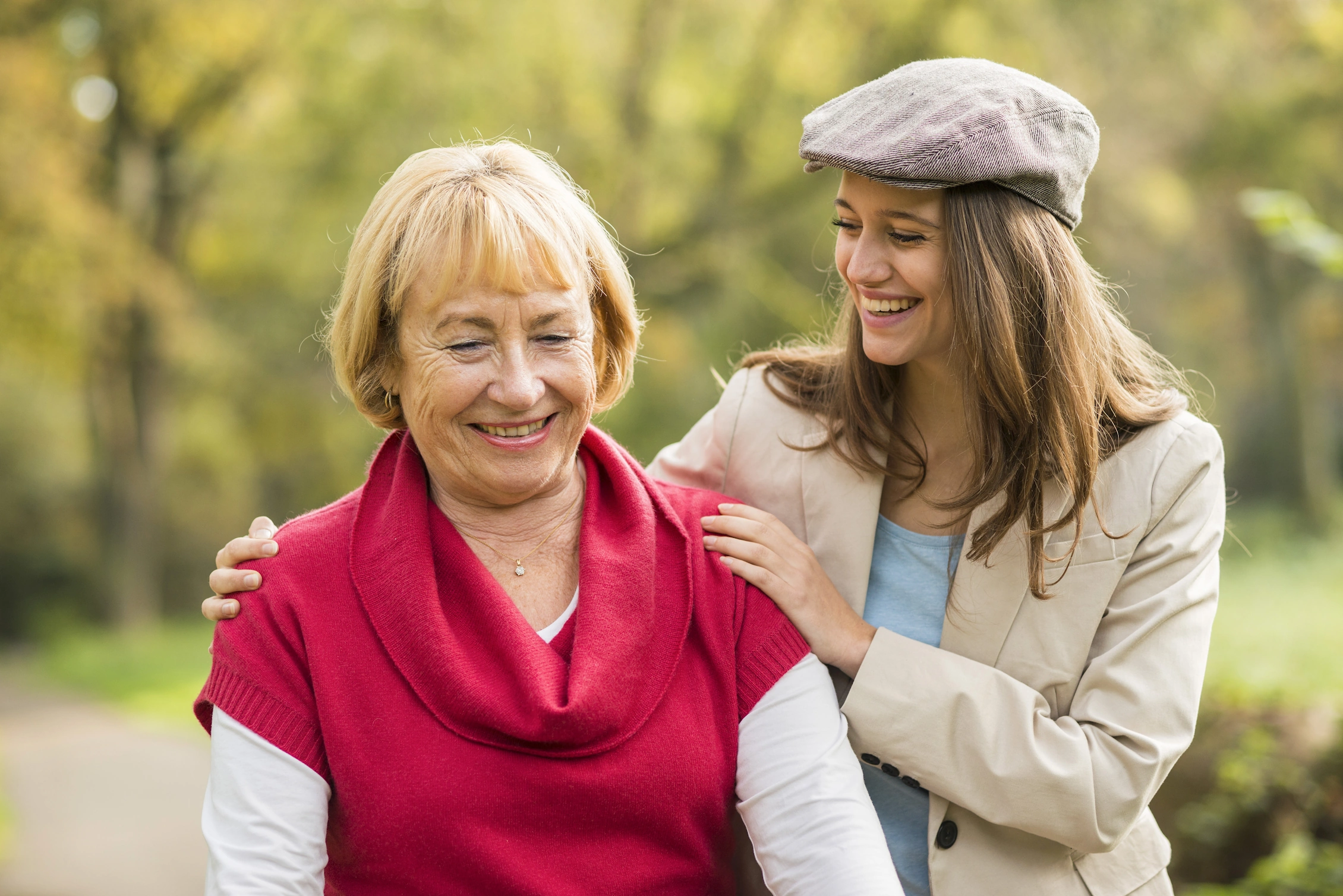 Smiling senior woman enjoys a warm outdoor moment with a caring loved one by her side.
